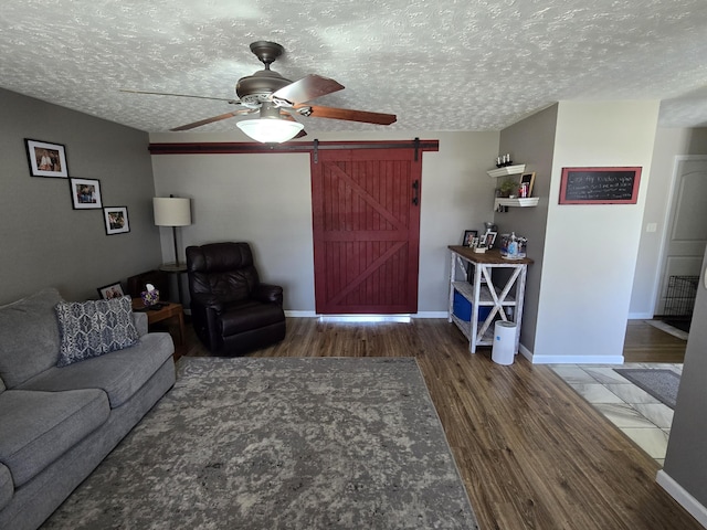 living area with a barn door, baseboards, ceiling fan, wood finished floors, and a textured ceiling