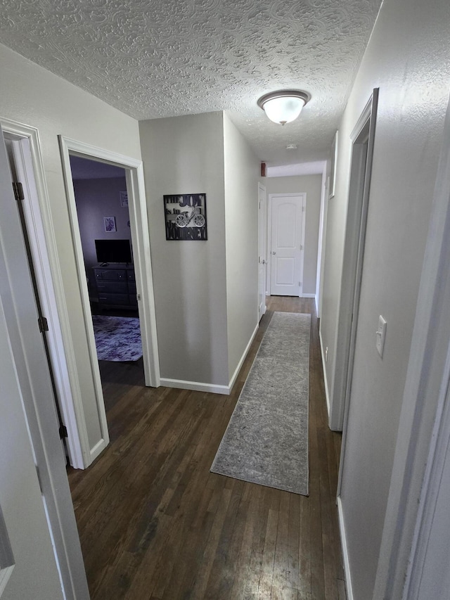 corridor with dark wood-style flooring, a textured ceiling, and baseboards