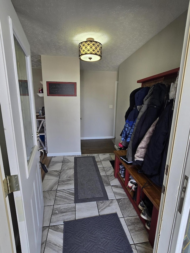 mudroom featuring marble finish floor, a textured ceiling, and baseboards