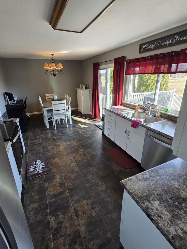 kitchen featuring baseboards, white cabinets, dishwasher, dark countertops, and a sink