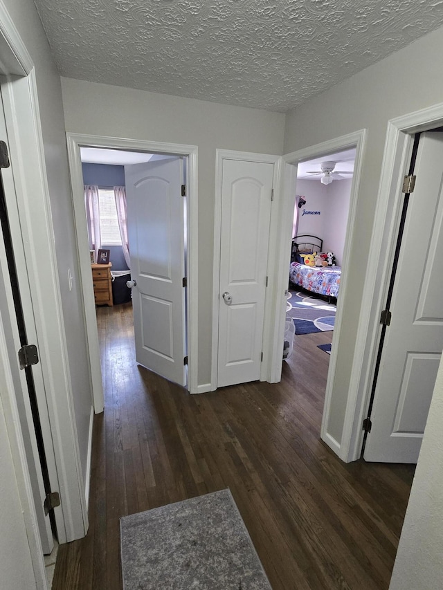 hallway with a textured ceiling, baseboards, and dark wood-style flooring