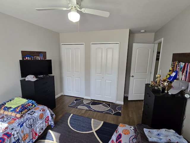 bedroom with a ceiling fan, wood finished floors, baseboards, and two closets