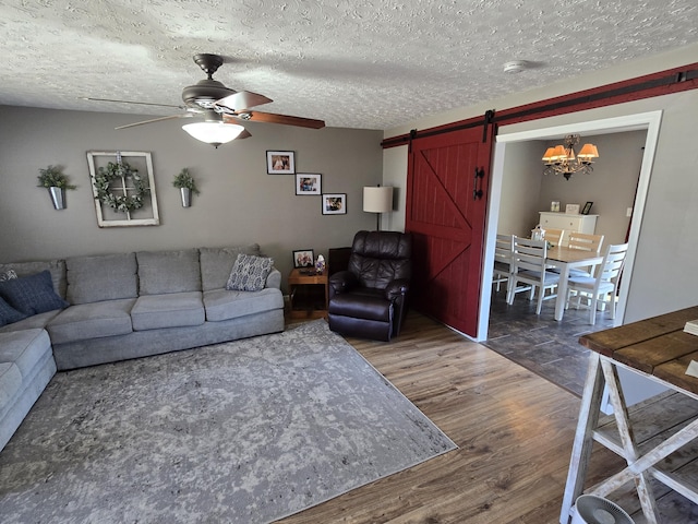 living room with a barn door, a textured ceiling, ceiling fan, and wood finished floors