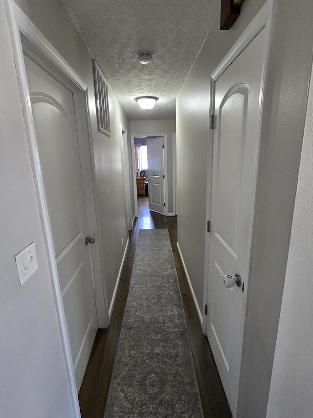 hallway with visible vents, a textured ceiling, baseboards, and dark wood-type flooring