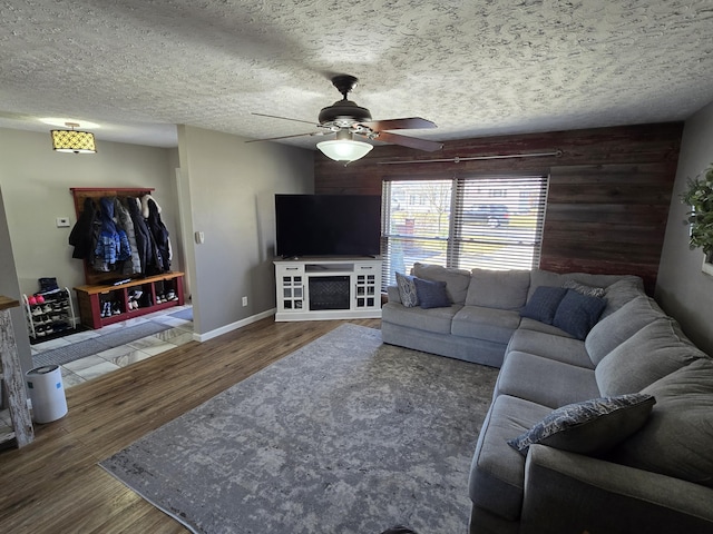 living area with a textured ceiling, ceiling fan, wood walls, wood finished floors, and baseboards