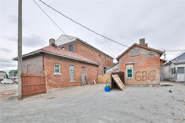 back of property featuring a chimney, metal roof, brick siding, and fence