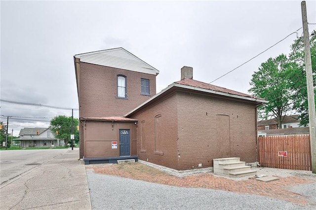 exterior space with brick siding, a chimney, and fence