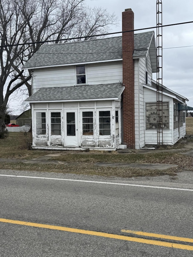 view of front facade featuring a shingled roof and a chimney