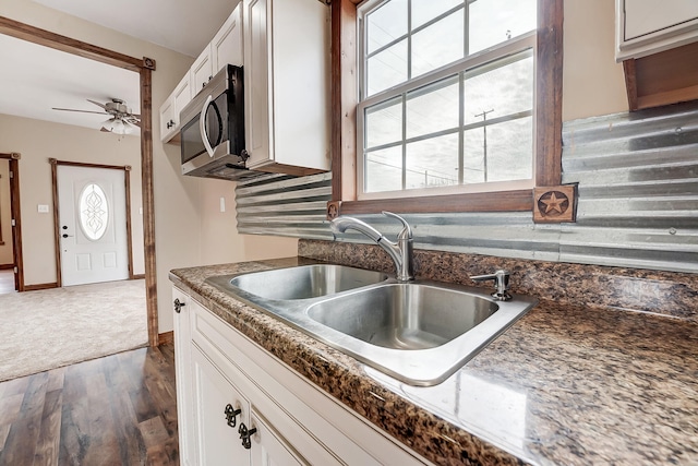 kitchen with a sink, stainless steel microwave, dark countertops, dark wood finished floors, and white cabinets