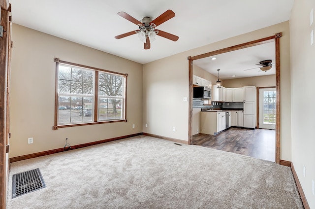 unfurnished living room with visible vents, baseboards, a ceiling fan, and dark carpet