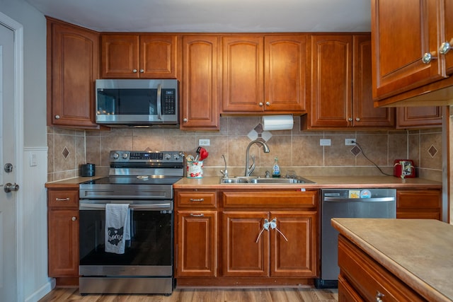 kitchen featuring brown cabinetry, stainless steel appliances, light countertops, and a sink