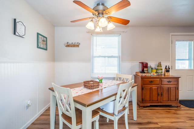 dining area with ceiling fan, light wood-style flooring, and wainscoting