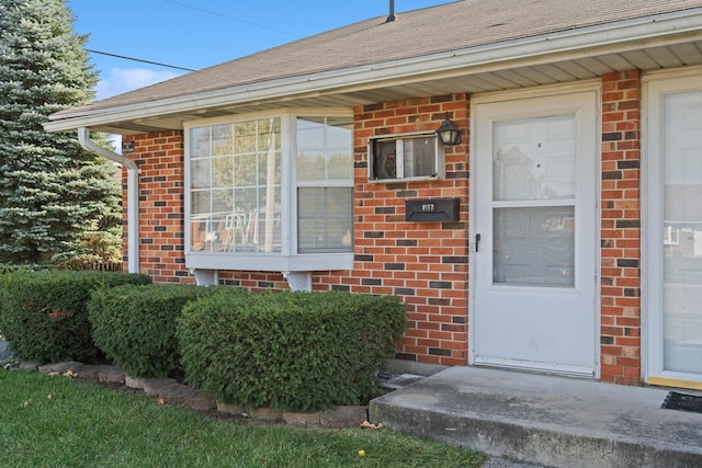 doorway to property featuring a garage, brick siding, and roof with shingles