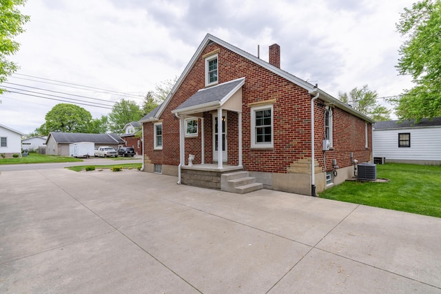 704 Campbell Rd, Sidney, OH 45365 - bungalow featuring central air condition unit, a chimney, brick siding, and a front yard