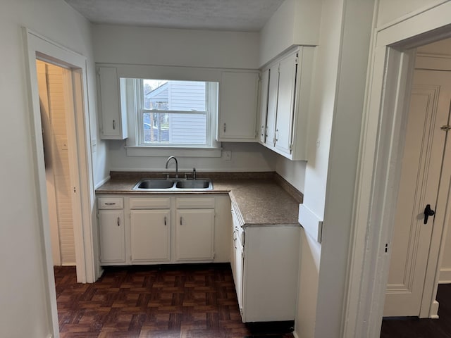 kitchen featuring dark parquet flooring, sink, a textured ceiling, and white cabinets