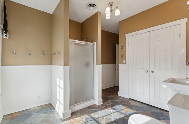 full bathroom with a wainscoted wall, a closet, visible vents, a stall shower, and stone finish floor