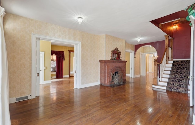 unfurnished living room featuring arched walkways, a fireplace, wood-type flooring, visible vents, and stairs