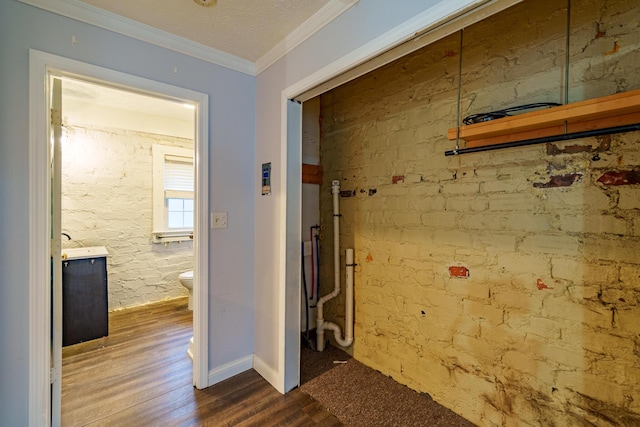 hallway with brick wall, wood finished floors, and crown molding