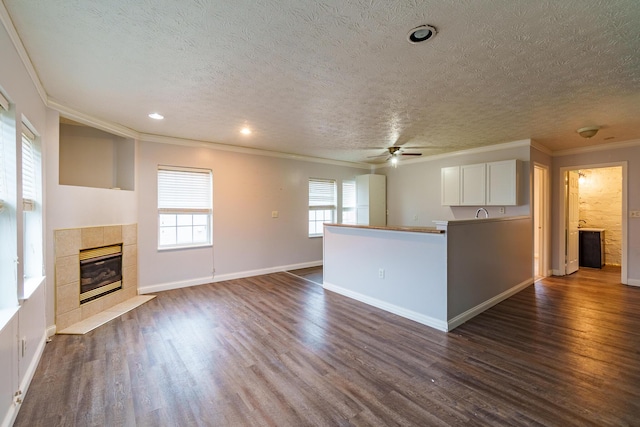 unfurnished living room featuring a textured ceiling, baseboards, dark wood-style floors, a tiled fireplace, and crown molding