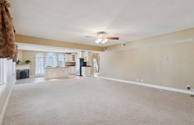 unfurnished living room with arched walkways, light carpet, a fireplace, visible vents, and baseboards