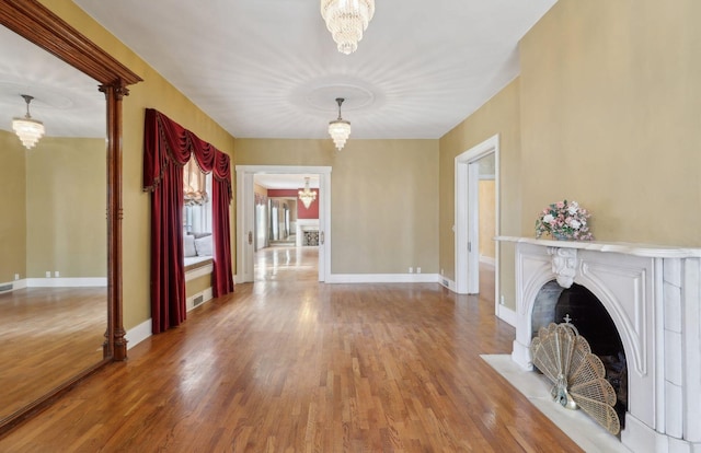 interior space with an inviting chandelier, a fireplace with flush hearth, baseboards, and wood finished floors