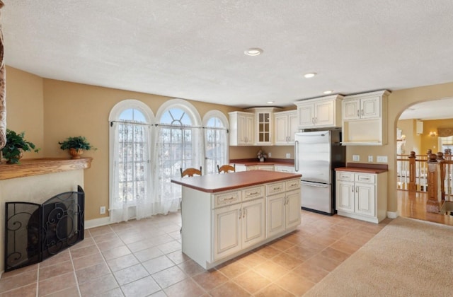 kitchen with arched walkways, freestanding refrigerator, cream cabinetry, and glass insert cabinets