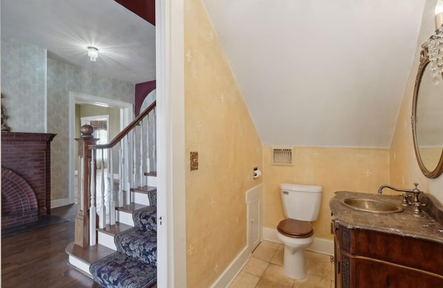 bathroom featuring visible vents, toilet, vaulted ceiling, vanity, and a brick fireplace