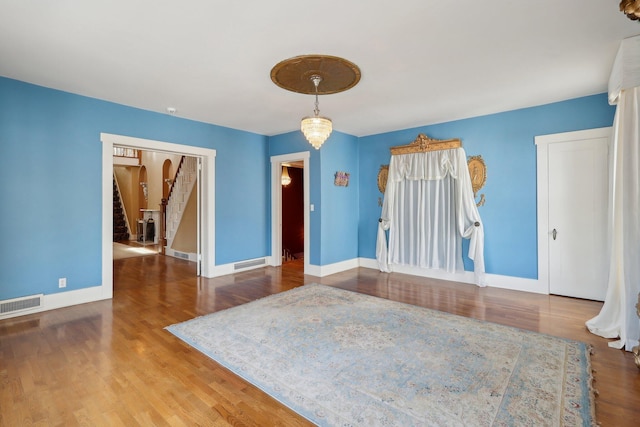 spare room featuring an inviting chandelier, baseboards, visible vents, and wood finished floors