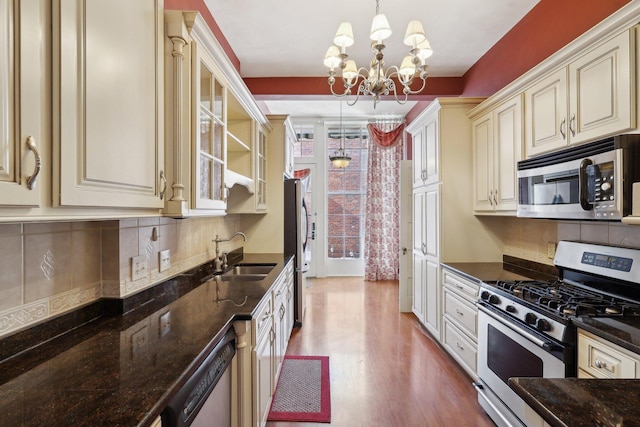 kitchen with decorative light fixtures, stainless steel appliances, a sink, cream cabinetry, and glass insert cabinets