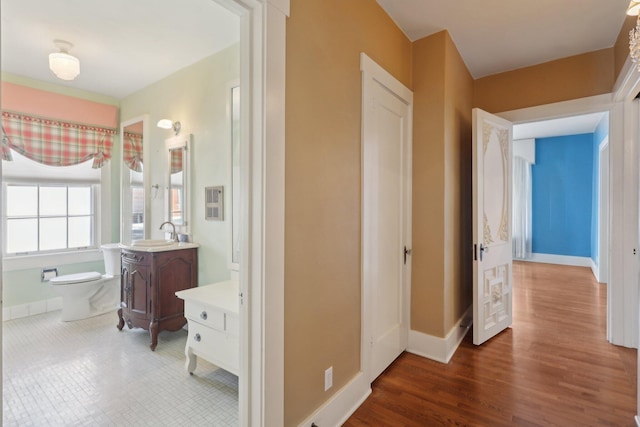 corridor with dark wood-style floors, baseboards, and a sink