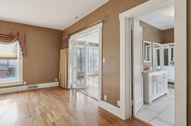 empty room with light wood-type flooring, visible vents, a sink, and baseboards