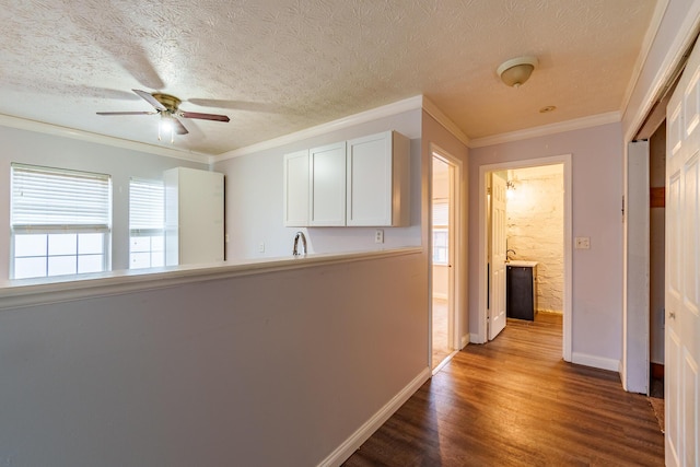 corridor with ornamental molding, a textured ceiling, baseboards, and wood finished floors