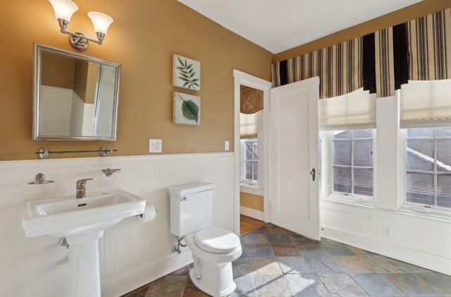 bathroom featuring stone finish flooring, a wainscoted wall, and toilet