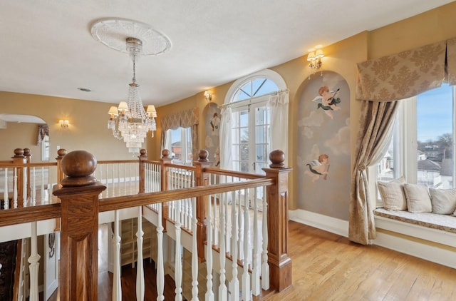 hall with light wood-style floors, baseboards, a notable chandelier, and an upstairs landing