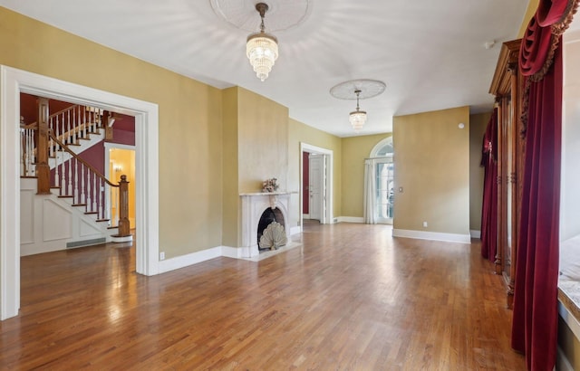 unfurnished living room with a fireplace with flush hearth, stairs, baseboards, and wood finished floors