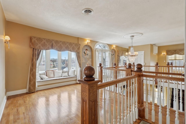 hall with light wood finished floors, baseboards, visible vents, a textured ceiling, and a chandelier