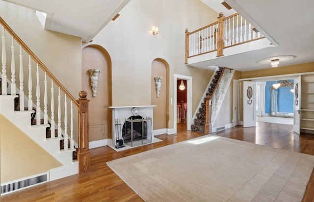 unfurnished living room featuring a fireplace, wood finished floors, a towering ceiling, visible vents, and stairs