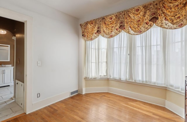 unfurnished dining area featuring light wood-type flooring, a sink, visible vents, and baseboards