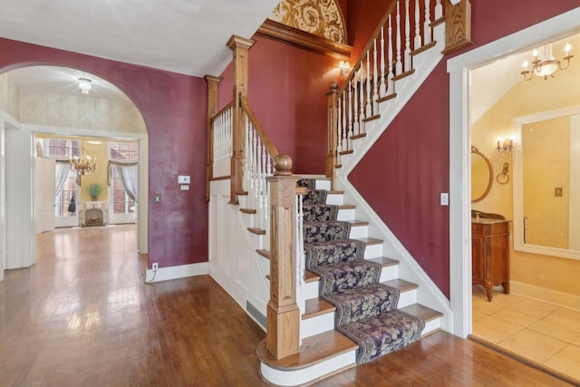 stairs with baseboards, a chandelier, arched walkways, and wood finished floors