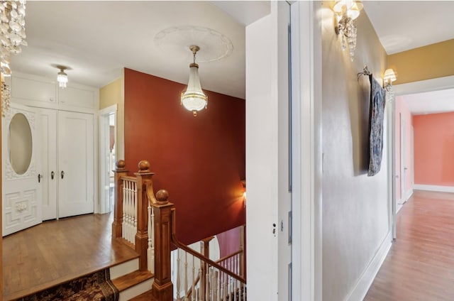 hallway featuring wood finished floors, an upstairs landing, and baseboards