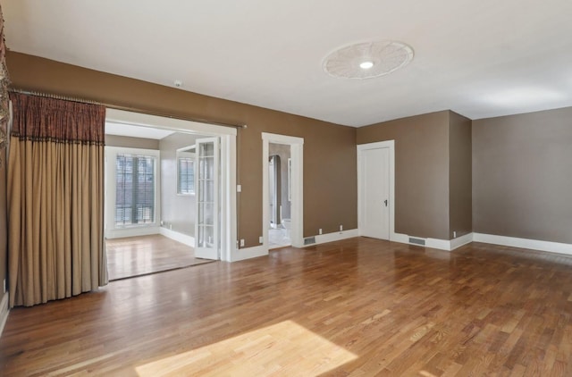 unfurnished room featuring baseboards, visible vents, and wood finished floors