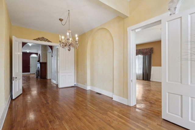 unfurnished dining area featuring arched walkways, a decorative wall, wood finished floors, and an inviting chandelier