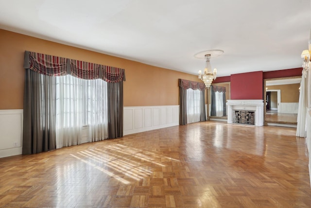 unfurnished living room featuring a wealth of natural light, a wainscoted wall, a fireplace, and a notable chandelier