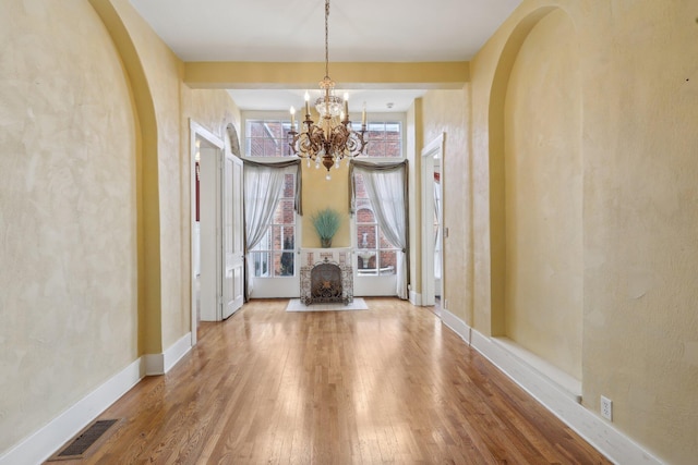 unfurnished dining area featuring arched walkways, visible vents, baseboards, hardwood / wood-style floors, and an inviting chandelier