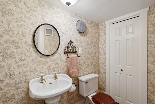 bathroom with a closet, visible vents, toilet, a sink, and wallpapered walls