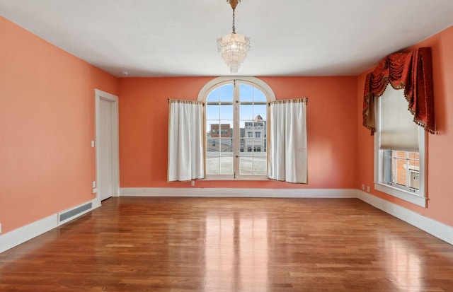 empty room featuring an inviting chandelier, visible vents, baseboards, and wood finished floors