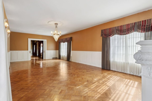 unfurnished room featuring a chandelier and a wainscoted wall