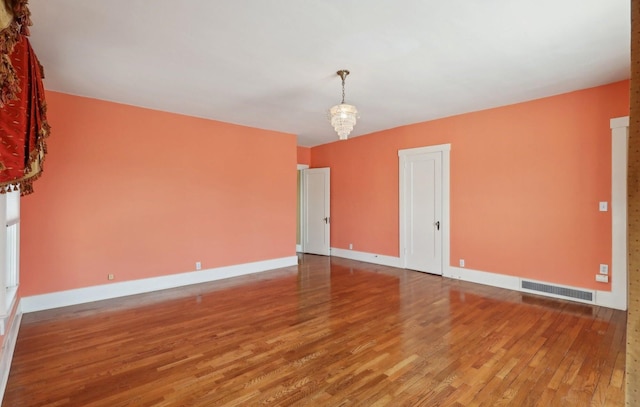 unfurnished room featuring a notable chandelier, baseboards, visible vents, and wood finished floors