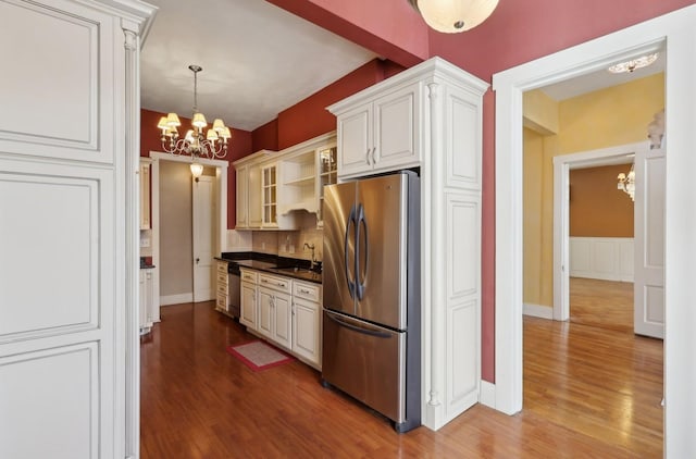 kitchen with dark countertops, glass insert cabinets, stainless steel appliances, a chandelier, and a sink