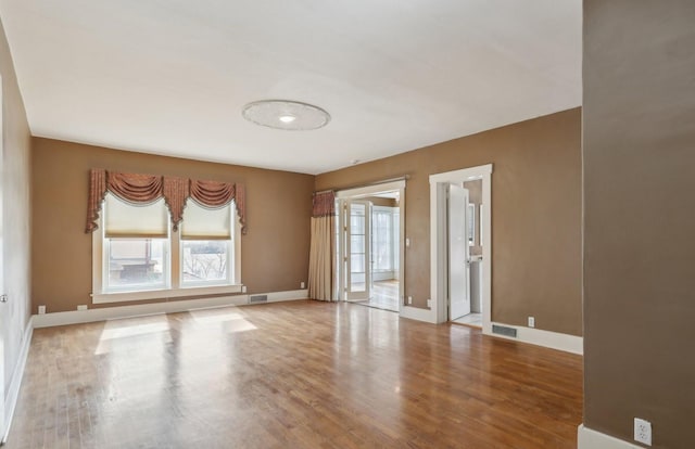 empty room featuring wood finished floors, visible vents, and baseboards